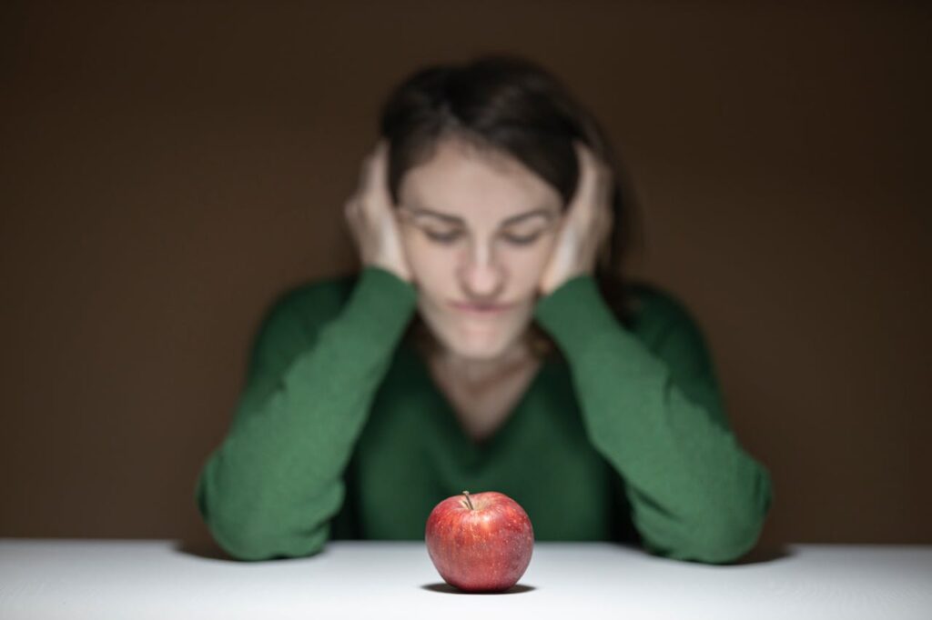 Crafting Captivating Headlines: Your awesome post title goes here A woman in a green sweater observes an apple on a table, creating a thoughtful scene.